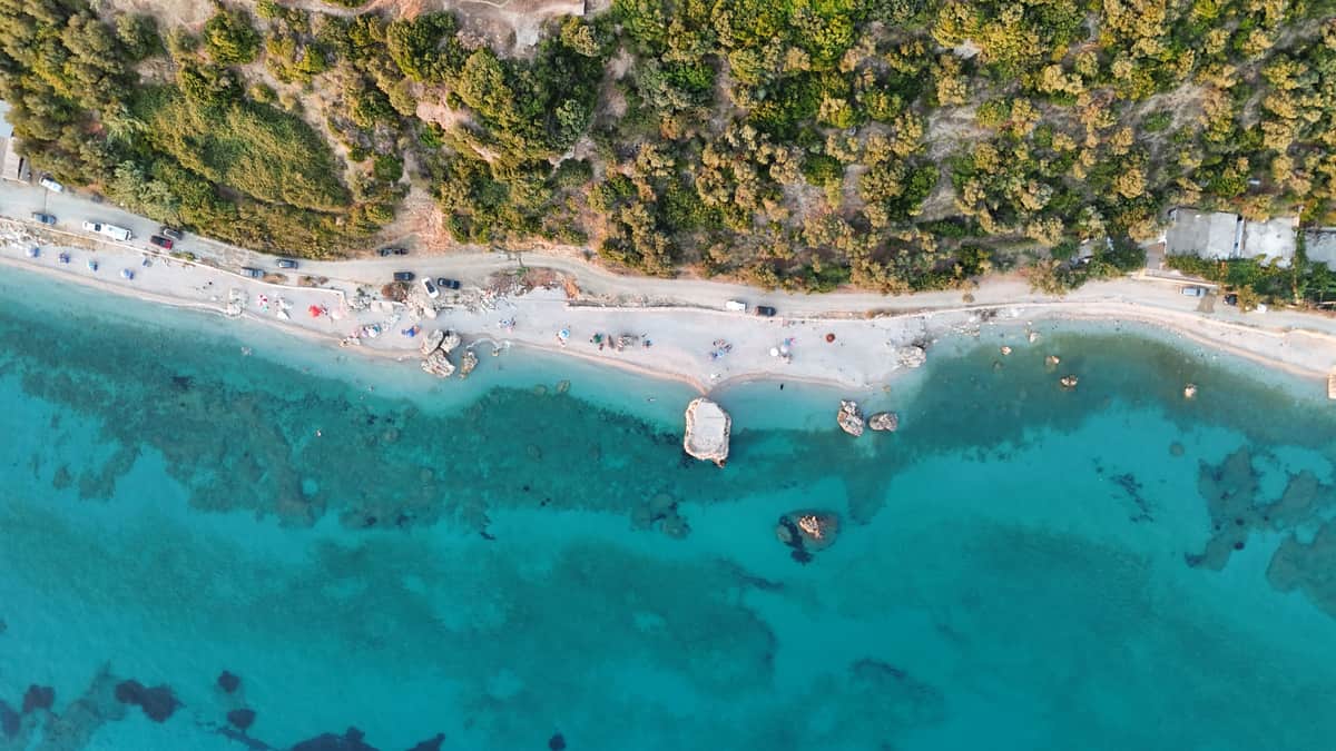 Vista aerea di una spiaggia di ciottoli con acqua turchese e la strada costiera sulla Riviera albanese